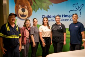 Six people posing in front of a Children's Hospital mural.
