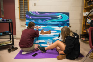 Two artists sitting on the floor to work on an Arctic themed mural.