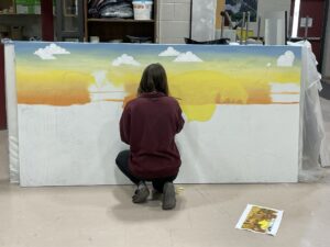 An artist squatting to work on a large unfinished mural,