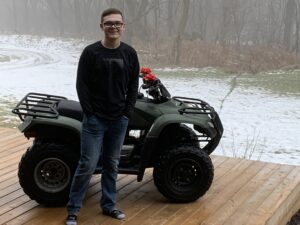 A teen standing in front of a quad bike with a bow on it.