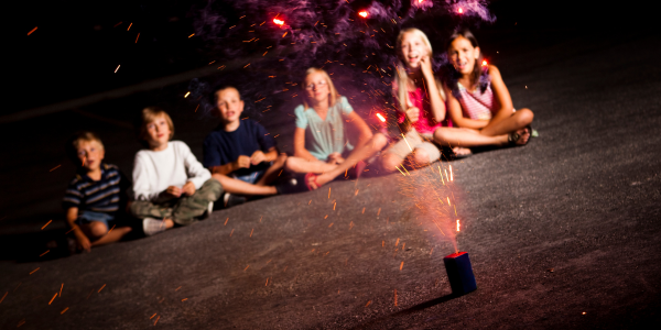 A group of kids sitting on the ground while a firework goes off in front of them