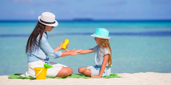 A mom applying sunscreen to her daughter's arm at the beach
