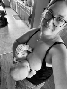 A black-and-white image of a new mom wearing glasses holding her infant as she breastfeeds.