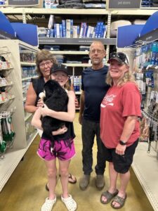 In the aisle of a pet store, a woman stands behind a child holding a puppy, while the child's mother and father stand to their side.