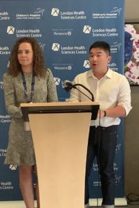 A curly-haired female doctor and a male radiologist stand and speak at a lectern.