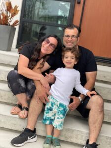 A mother, father and son sit together on the front steps of their house, smiling.