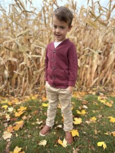 A boy in a red shirt standing in front of a dry, brown corn field in autumn.