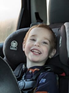 A child in a car seat smiling broadly.