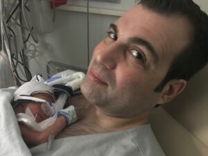 A father smiling slightly as he holds his tiny infant to his chest.