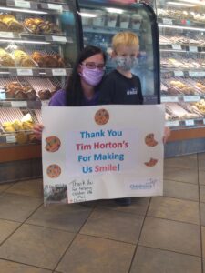 A mother and her son, both wearing face masks, pose while holding up a poster celebrating DQ Miracle Treat Day.